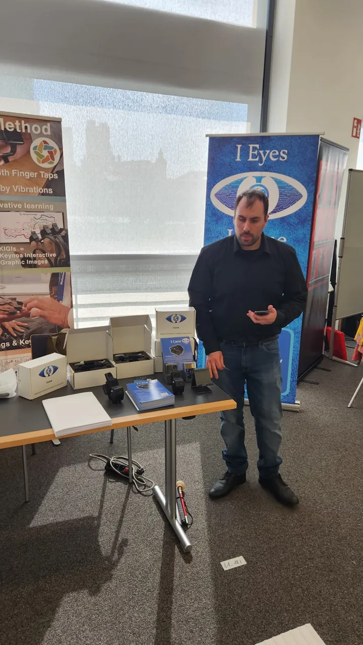 Kévin Derome debout devant le kakemono IEyes, à côté d'une table présentant des boîtiers ICane, leurs boîtes et des brochures.